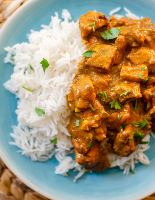 A plate with rice and slow cooker butter chicken with cilantro sprinkled on top