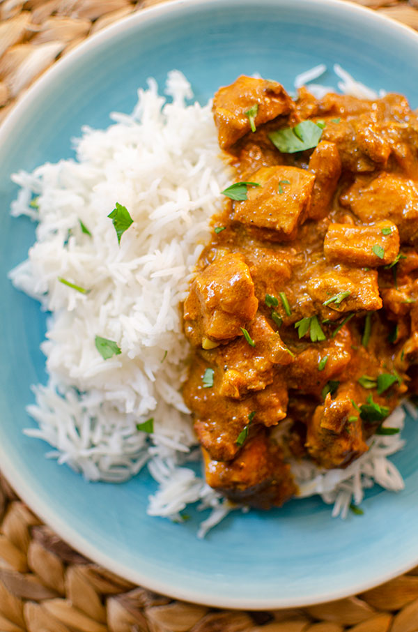 A plate with rice and slow cooker butter chicken with cilantro sprinkled on top