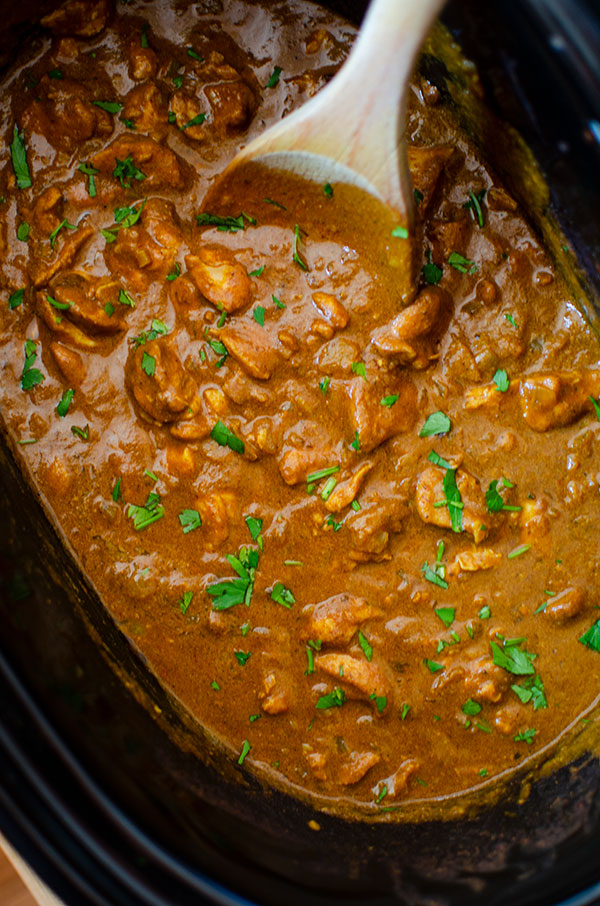 Butter chicken in the slow cooker insert with a wooden spoon