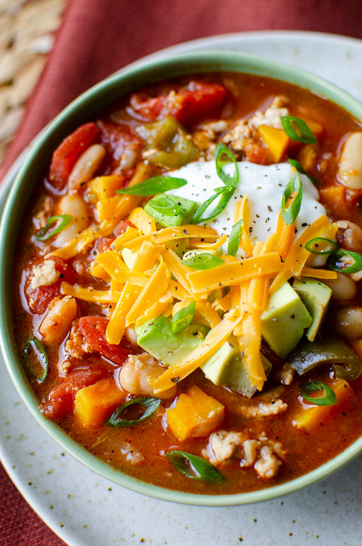 Closeup side angle of turkey white bean chili in a green bowl on a white plate.