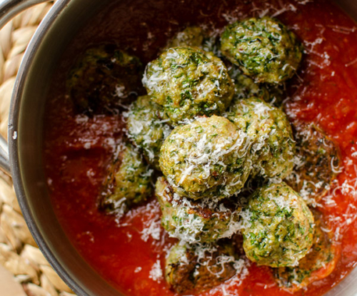 Turkey spinach meatballs in marinara sauce in a pot with parmesan cheese on top.