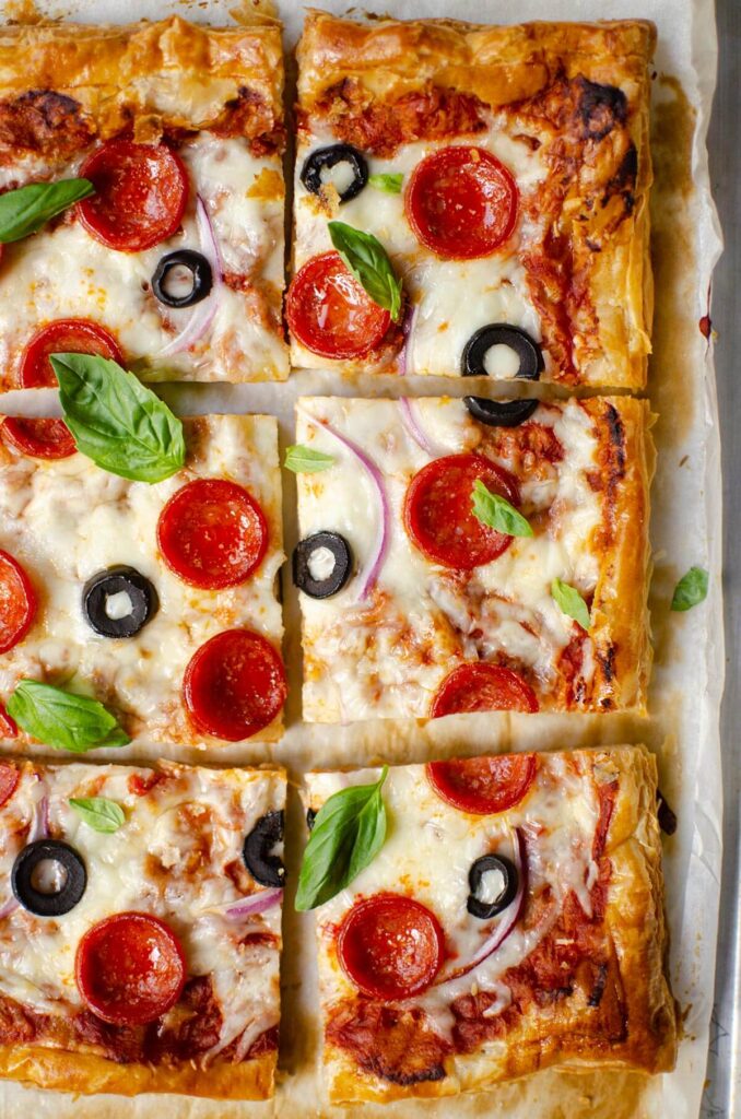 Puff pastry pizza cut into slices on a baking sheet with parchment paper.