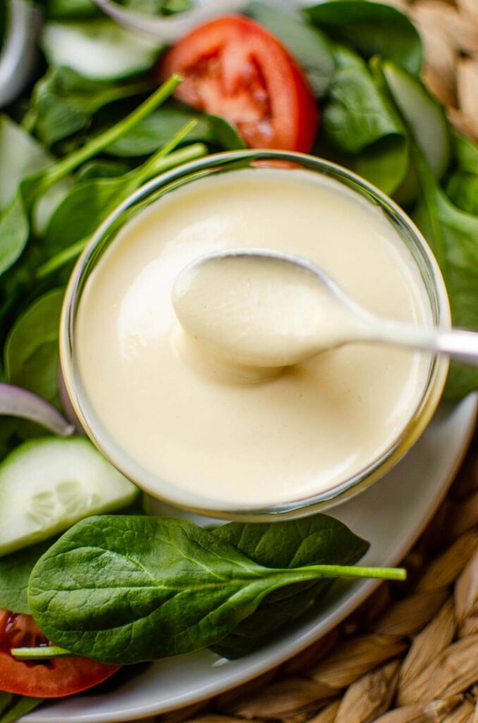 Closeup of a spoon in the dressing with a salad on the side.