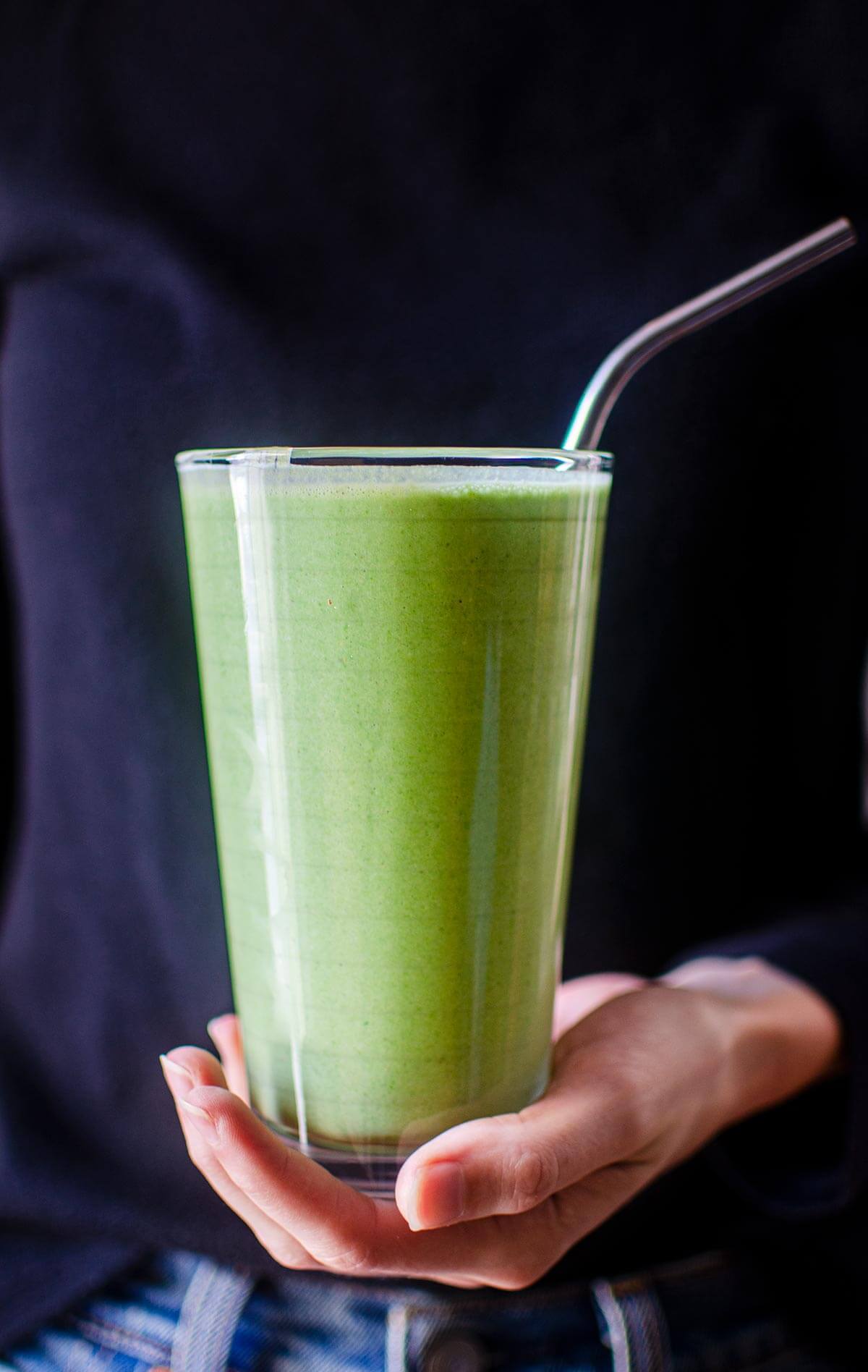A person holding a glass of spinach banana smoothie