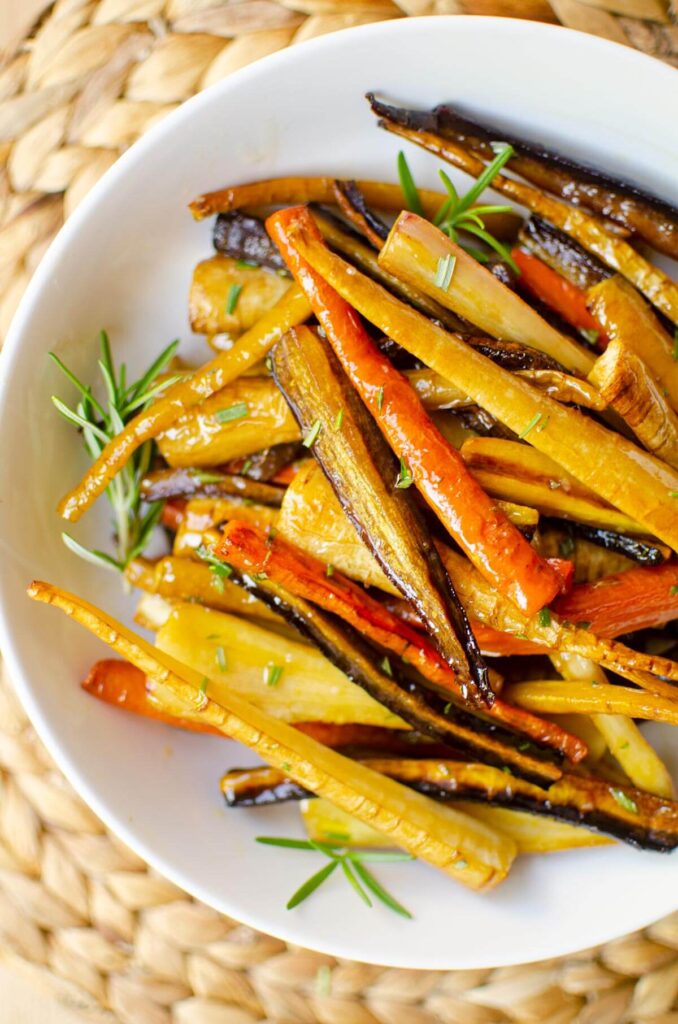 Closeup of roasted carrots and parsnips in a white bowl with rosemary.
