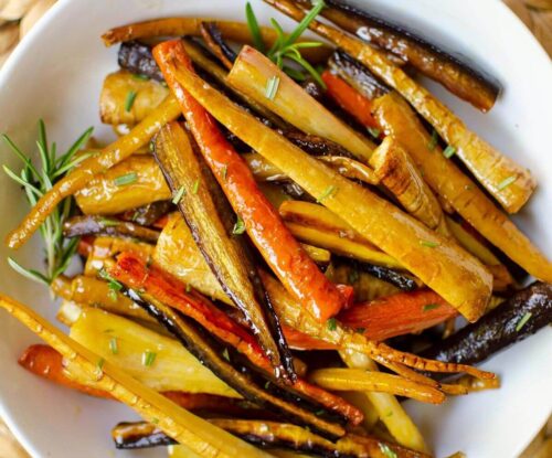 Closeup of vegetables in a white bowl with fresh rosemary sprinkled on top.
