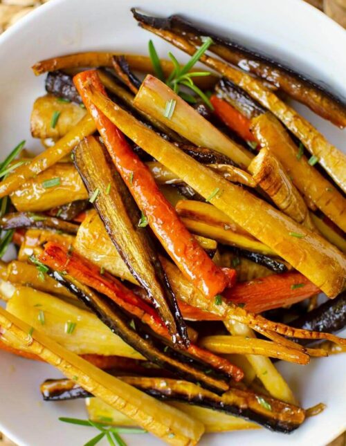 Closeup of vegetables in a white bowl with fresh rosemary sprinkled on top.