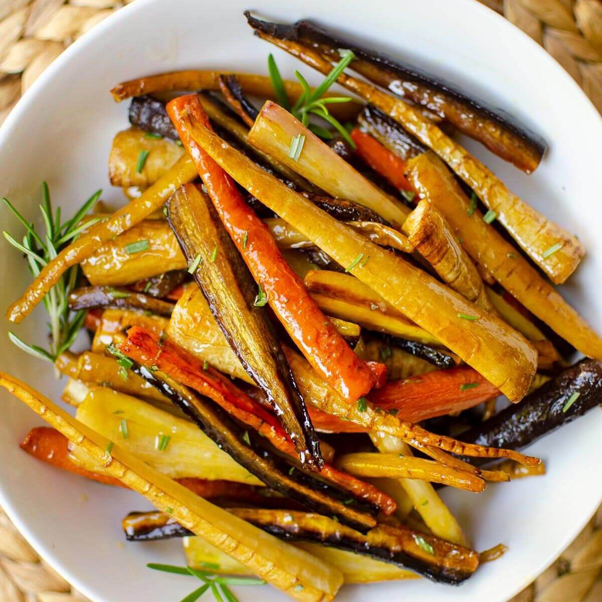 Closeup of vegetables in a white bowl with fresh rosemary sprinkled on top.