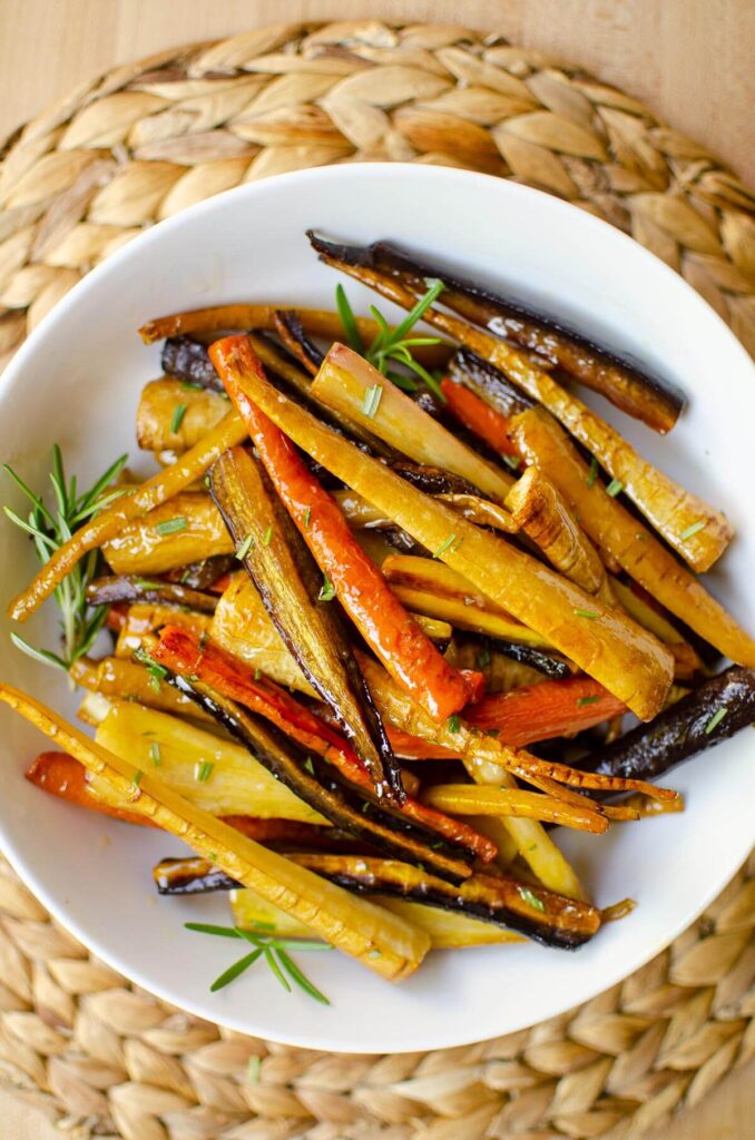 Roasted carrots and parsnips in a white bowl with fresh rosemary sprinkled on top.