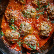 Beef meatballs in slow cooker with tomato sauce and basil.