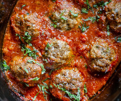 Beef meatballs in slow cooker with tomato sauce and basil.