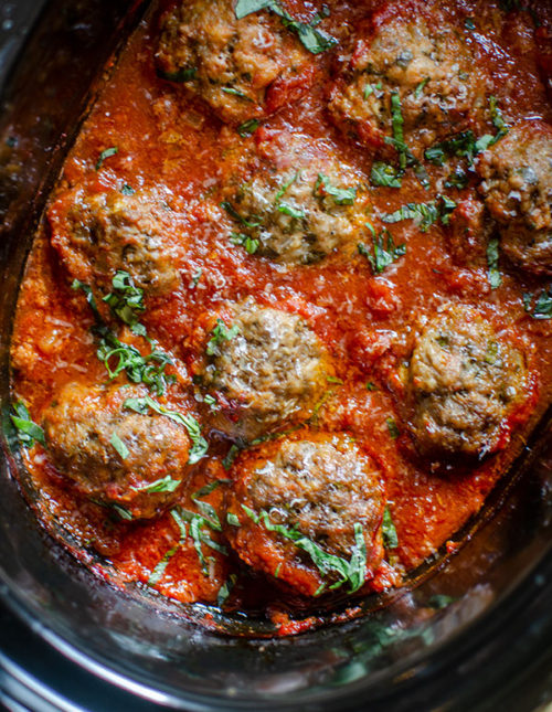 Beef meatballs in slow cooker with tomato sauce and basil.