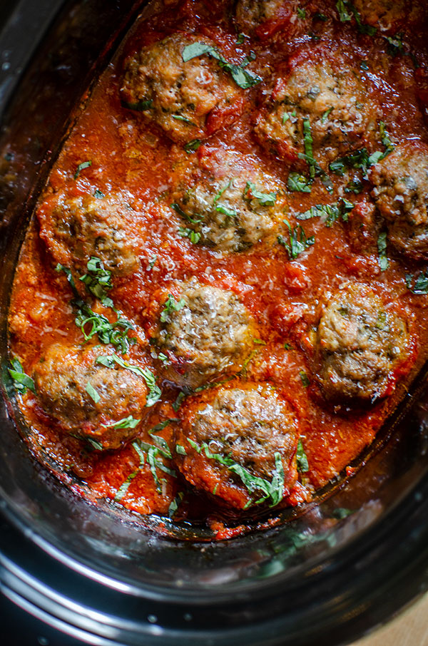 Beef meatballs in slow cooker with tomato sauce and basil.