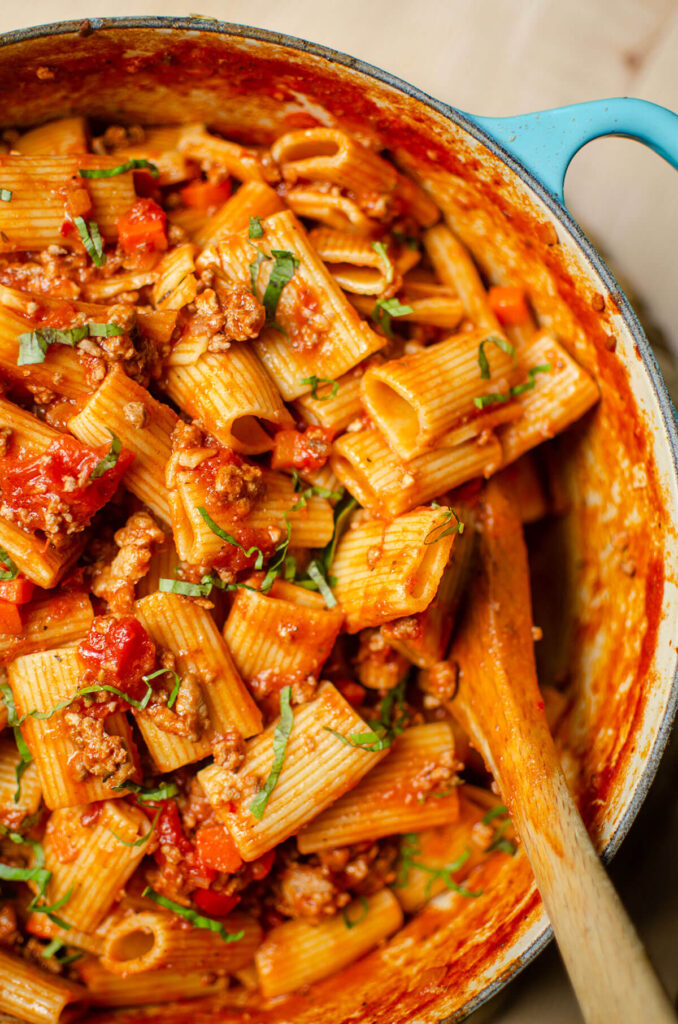 Closeup of rigatoni bolognese being stirred by a wooden spoon.