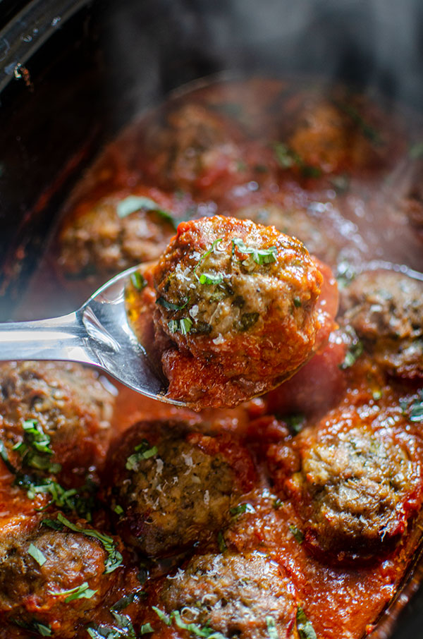 Closeup of slow cooker meatballs on a spoon with basil sprinkled on top.