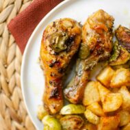 Closeup of chicken drumsticks on a white plate with potatoes and Brussels sprouts.