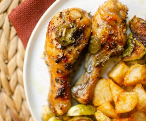 Closeup of chicken drumsticks on a white plate with potatoes and Brussels sprouts.