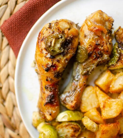 Closeup of chicken drumsticks on a white plate with potatoes and Brussels sprouts.