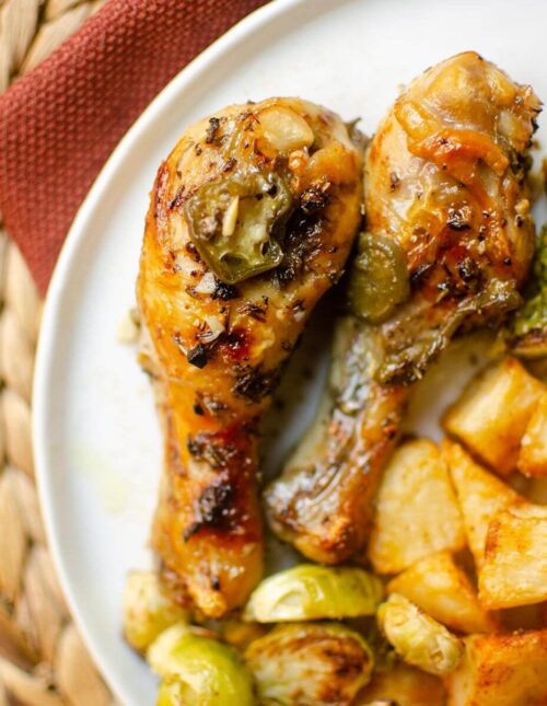 Closeup of chicken drumsticks on a white plate with potatoes and Brussels sprouts.