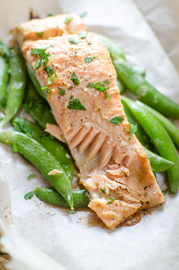 Cooked salmon fillet with a piece taken out of it served on top of sugar snap peas.