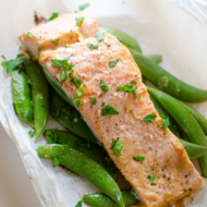 Cooked salmon on top of sugar snap peas in a parchment paper package.