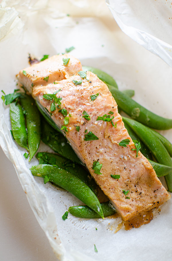Cooked salmon on top of sugar snap peas in a parchment paper package.