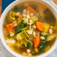 Six vegetable white bean soup in a white bowl on blue napkins.