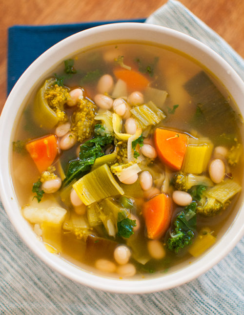 Six vegetable white bean soup in a white bowl on blue napkins.