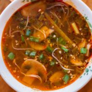 Spicy ginger scallion soup in a white bowl with a bowl of limes on the side.