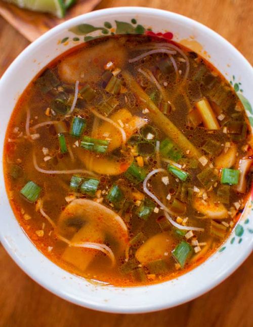 Spicy ginger scallion soup in a white bowl with a bowl of limes on the side.