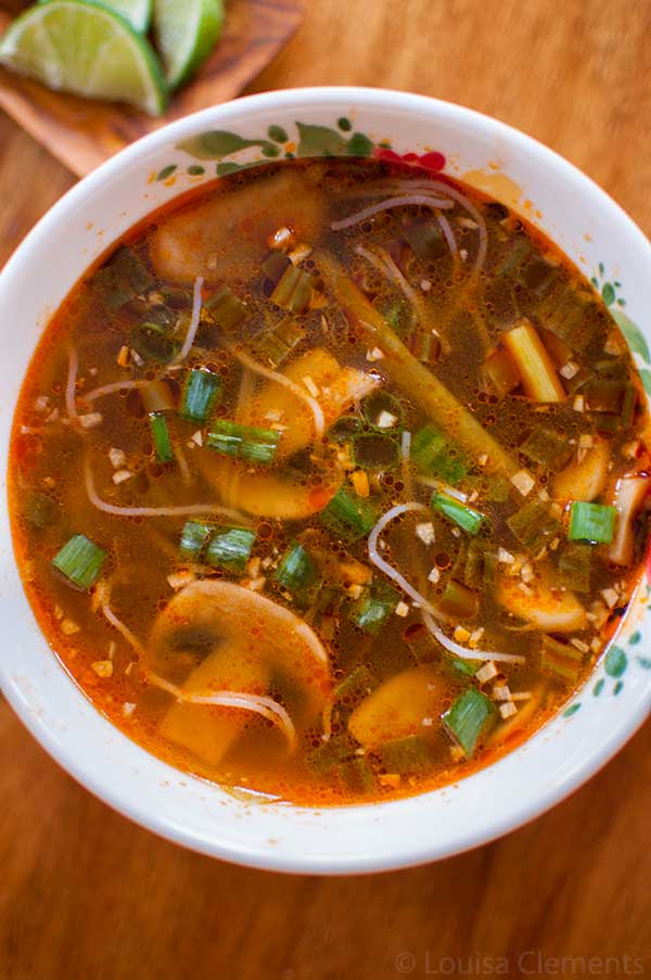 Spicy ginger scallion soup in a white bowl with a bowl of limes on the side.