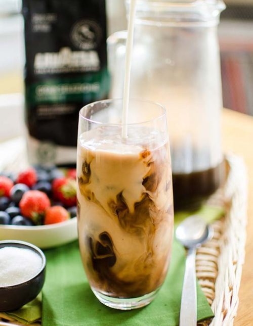 Milk being poured into iced coffee with mocha ice cubes