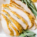 Closeup of sliced turkey on a platter with fresh sage garnish.