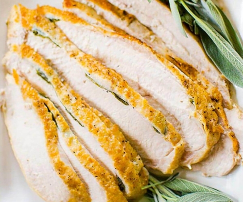 Closeup of sliced turkey on a platter with fresh sage garnish.