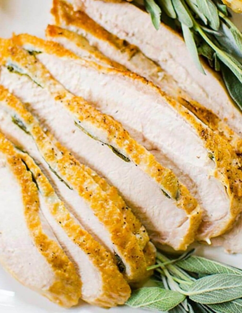 Closeup of sliced turkey on a platter with fresh sage garnish.