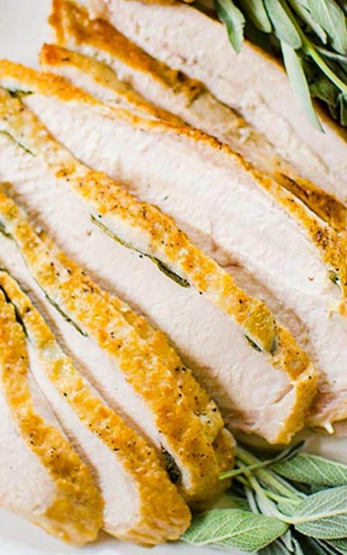 Closeup of sliced turkey on a platter with fresh sage garnish.