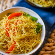 Vegetarian singapore noodles in a white bowl on a blue napkin
