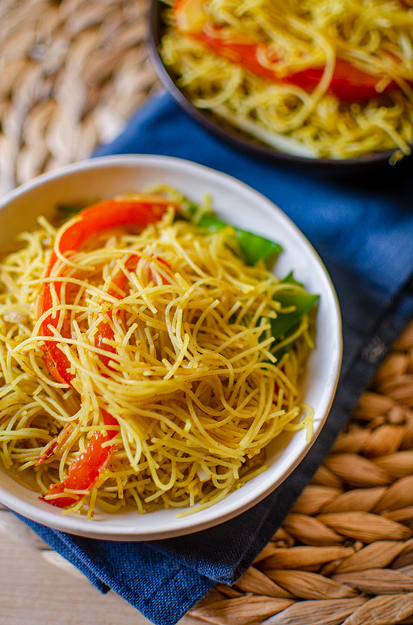 Vegetarian singapore noodles in a white bowl on a blue napkin