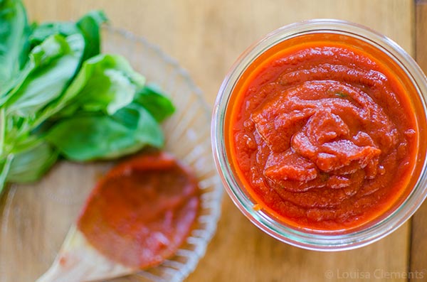 High angle of marinara sauce in a jar with fresh basil and a wooden spoon. 