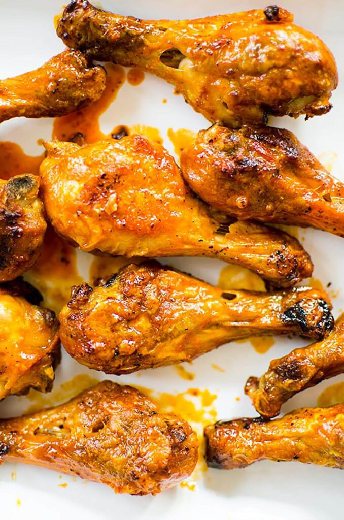 A white platter of Buffalo chicken drumsticks.