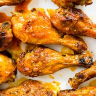 Closeup of cooked drumsticks tossed in Buffalo sauce on a white platter.