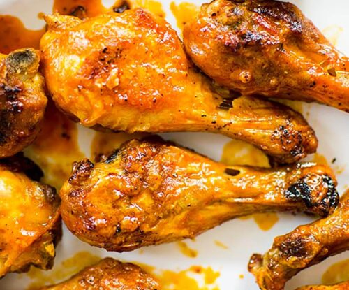 Closeup of cooked drumsticks tossed in Buffalo sauce on a white platter.