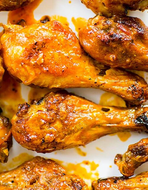 Closeup of cooked drumsticks tossed in Buffalo sauce on a white platter.