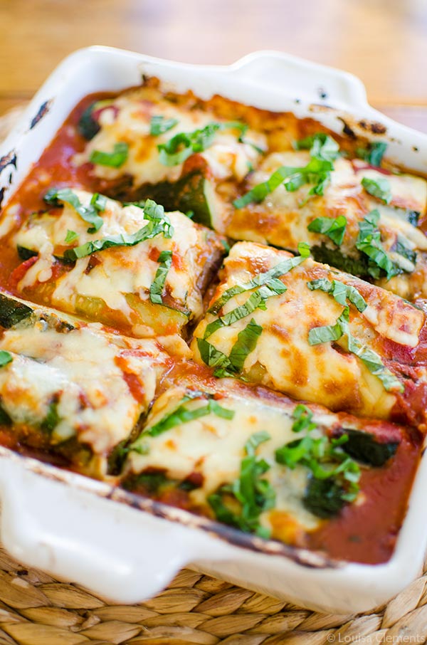 Zucchini and eggplant lasagna in a white baking dish with fresh basil on top.