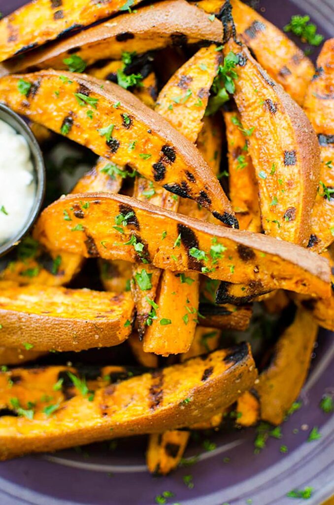 Closeup of grilled sweet potato fries on a purple plate with parsley sprinkled on top.