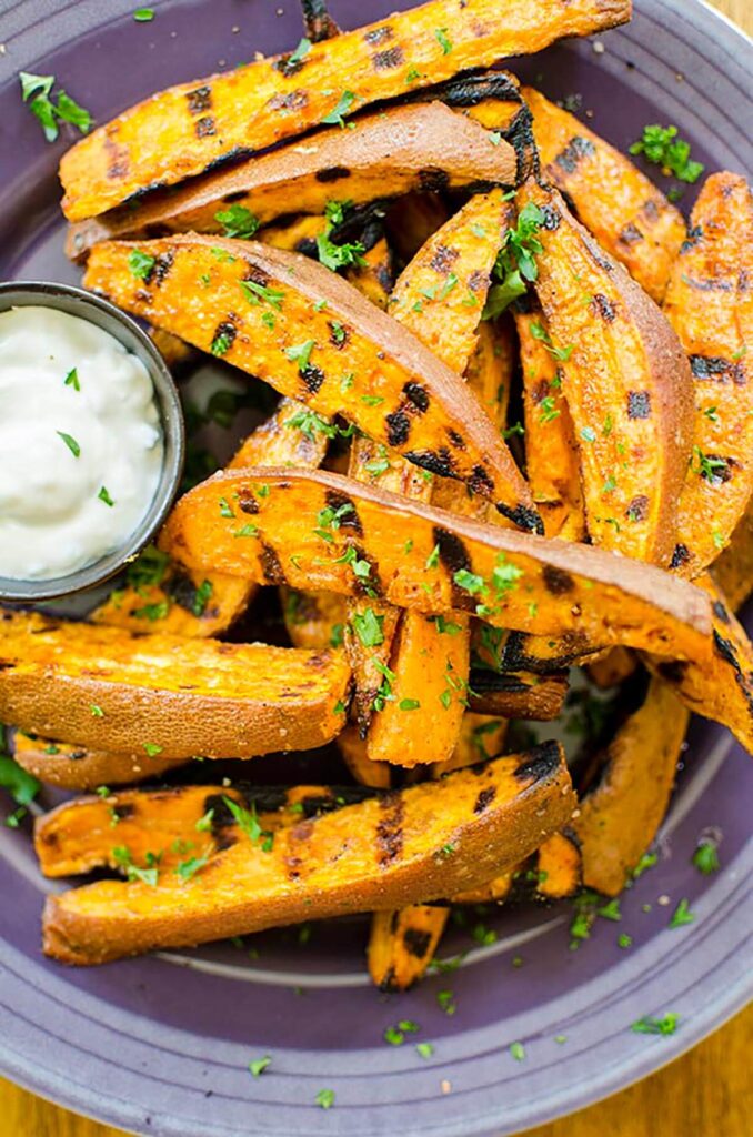 Grilled sweet potato fries on a purple plate with a garlic aioli.