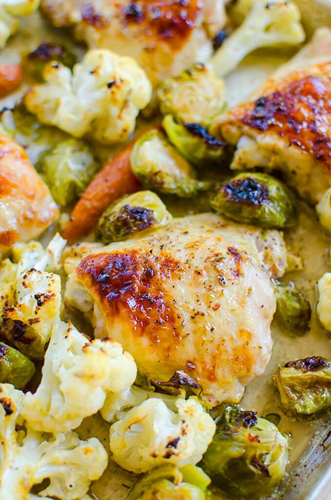 Closeup of roasted chicken thigh, roasted cauliflower, carrots and brussels sprouts.