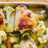 Closeup of one roasted chicken thigh with vegetables on a sheet pan.