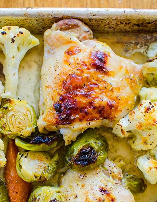 Closeup of one roasted chicken thigh with vegetables on a sheet pan.