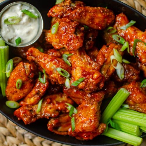 Closeup of chicken wings in a cast iron platter with celery and dip, with sliced green onions sprinkled on top.